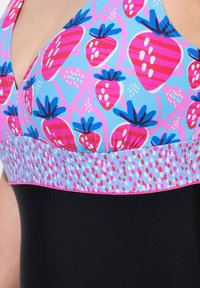 Enhelkelfärgad baddräkt med en blå överdel prydd med rosa och röda jordgubbsmönster, ett kontrasterande band med prickdesign, och en svart underdel.