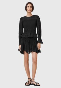 Abito nero con maniche lunghe, corpino smockato, vita peplum e gonna a strati. Realizzato in tessuto leggero, presenta una texture leggermente trasparente.