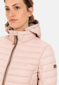 Veste matelassée rose clair avec fermeture éclair, col montant et capuche réglable. Dotée d'un patch logo sur la manche et de coutures horizontales.