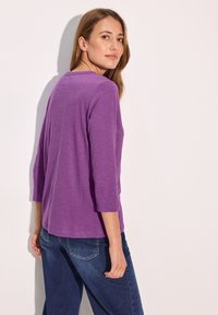 Lila Langarmshirt mit entspannter Passform und Rundhalsausschnitt, kombiniert mit blauen Jeans. Der Stoff wirkt weich und leicht.