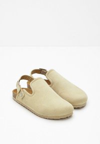 Chaussures slingback en suède beige avec un bout rond, une sangle réglable et une semelle texturée pour une meilleure adhérence. Design simple sans motifs marquants.