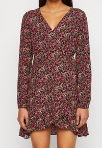 Blumenkleid mit tiefem V-Ausschnitt, langen Ärmeln und einem gepufften Saum. Das Stoffmuster umfasst rosa, grüne und weiße Blumen auf schwarzem Hintergrund.