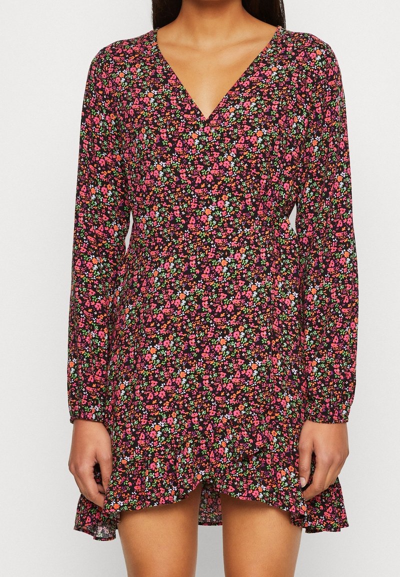 Blumenkleid mit tiefem V-Ausschnitt, langen Ärmeln und einem gepufften Saum. Das Stoffmuster umfasst rosa, grüne und weiße Blumen auf schwarzem Hintergrund.