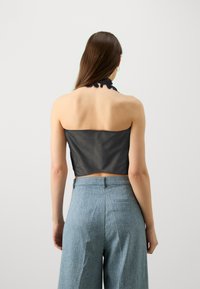 Top corto negro con diseño de cuello halter texturizado, combinado con pantalones anchos de corte recto en azul claro con un acabado suave y bolsillo en la parte trasera.