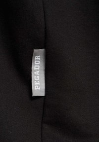 Melnas audums ar gludu tekstūru, kurā ir pelēks birku ar uzrakstu "PEGADOR" treknā fontā, izvietota gar malām.