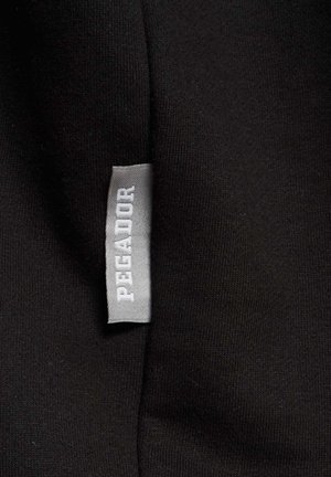 Fekete szövet, sima felülettel, egy szürke címkét tartalmaz, amelyen vastag betűkkel a "PEGADOR" felirat található, az anyag szélén elhelyezve.