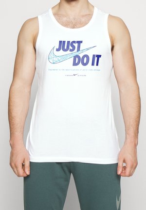 Man in een witte mouwloze Nike-shirt met "JUST DO IT" en een grafisch swoosh-ontwerp, gecombineerd met donkergroene trainingsbroek.