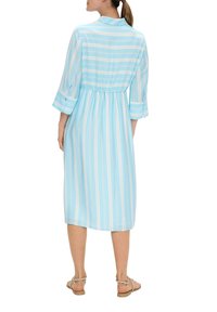 Hellblaues Midi-Kleid mit weißen vertikalen Streifen, geknöpften Ärmelbündchen, Kragen und gerafftem Bund. Getragen mit flachen Sandalen.