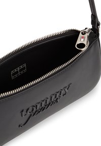 Μαύρο δερμάτινο μικρό τσαντάκι χειρός με ανάγλυφο λογότυπο Tommy Jeans, ασημένιο φερμουάρ μερικώς ανοιχτό και λογότυπο στην τρύπα του φερμουάρ.