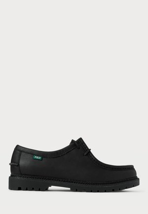Zapato de cuero negro con perfil bajo, punta redonda y suela texturizada. Presenta una etiqueta verde "POLO" y costuras en contraste a lo largo del borde.