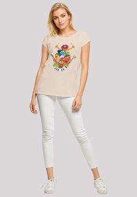 Beige cotton t-shirt with a colorful graphic featuring cartoon characters and a piano. Paired with white skinny jeans and white sneakers.