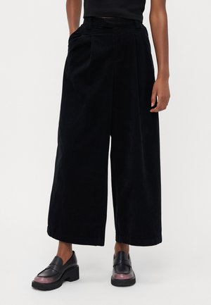 Sorte vide ben corduroy bukser med en tekstureret overflade, plisseret front, elastisk talje og sidelommer, parret med sorte loafers.
