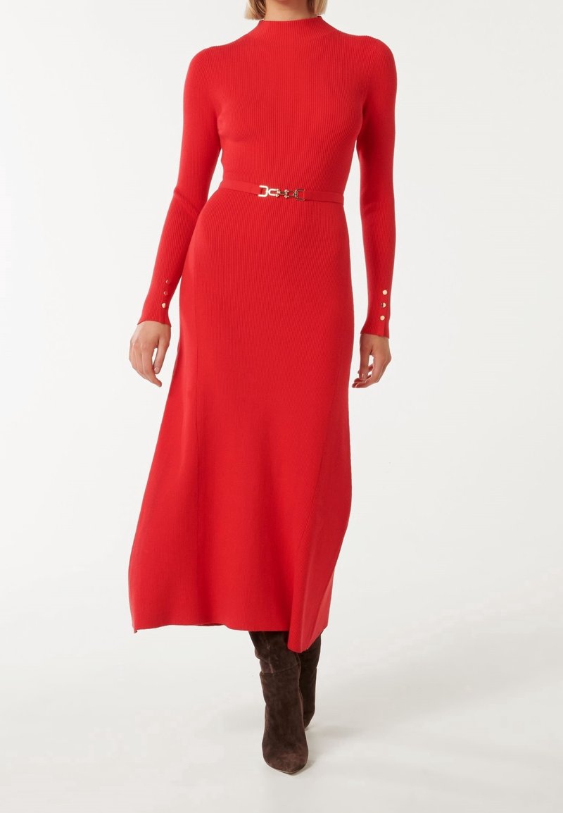 Femme portant une robe midi à manches longues en maille côtelée rouge avec une fine ceinture assortie et des bottes hautes en suède marron jusqu'aux genoux.
