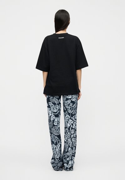 Μαύρο υπερμεγέθες μπλουζάκι με μικρό λευκό λογότυπο στην πλάτη, σε συνδυασμό με φαρδιά μπλε και λευκά παντελόνια με μοτίβα που περιστρέφονται.