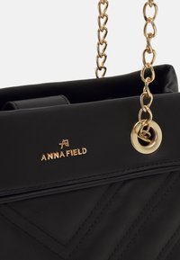 Sort læderhandtaske med en guldkædestropp, der har et quiltet design og en guldfarvet logoplade. Cirkelrunde grommet detalje synlig.