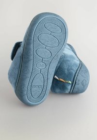 Des chaussons en peluche bleus avec une semelle en caoutchouc texturé, présentant une base plate et des accents en tissu. Taille indiquée comme 6 au bas.
