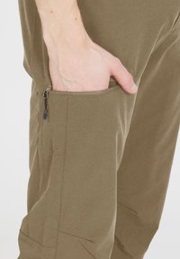 Olivgröna byxor i mjukt tyg, med en ficka på sidan som stängs med dragkedja och en strukturerad, åtsittande form med subtila sömnadsdetaljer.