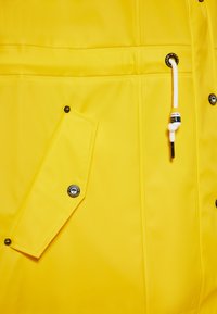 Geltona vandeniui atspari striukė su lygiu paviršiumi, spaudėmis sagomis, užtrauktuku užsegama kišenė ir suveržimo reguliavimu. Pabrėžia kontrastingi metaliniai akcentai.