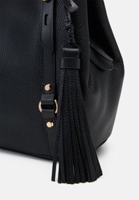 Sort læder håndtaske med en tekstureret overflade, guldfarvede metaldele og en lang sort kwastdetalje på siden.