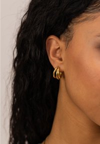 Goldene Ringohrringe mit einem Triple-Loop-Design und einer glatten, glänzenden Oberfläche, die ihre kreisrunde Form und eleganten Kurven betont.