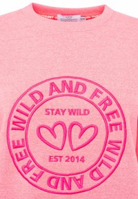 Rosa Sweatshirt mit einem runden gestickten Design, das "STAY WILD" und "MILD AND FREE" zeigt, akzentuiert durch zwei Herzformen in dunklerem Rosa.