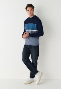 Tengerészkék pulóver kék, világoskék és fehér vízszintes csíkokkal; bordázott nyakkivágással és mandzsettákkal. Sötét farmernadrággal és fehér tornacipővel viselve.