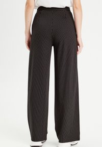 Pantalons larges noirs avec des rayures verticales blanches, dotés d'une taille haute et d'un tissu doux pour le confort. Comprend une ceinture cachée.