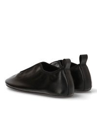 Zapatos negros de piel sin cordones con una textura suave, puntera en punta y lados elásticos, que cuentan con pequeñas lengüetas en el talón para ponérselos fácilmente.