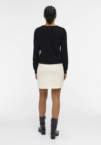 Sort langærmet sweater parret med en hvid miniskirt og sorte hælede støvler til midt på læggen. Glat materiale, tætsiddende design og minimal detaljer.