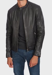 Svart läderjacka med quiltat axeldesign, slim fit, framficka med dragkedja och två sidofickor. Bärs över en mörk tröja och blå jeans.