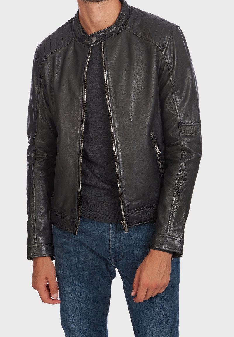 Svart läderjacka med quiltat axeldesign, slim fit, framficka med dragkedja och två sidofickor. Bärs över en mörk tröja och blå jeans.