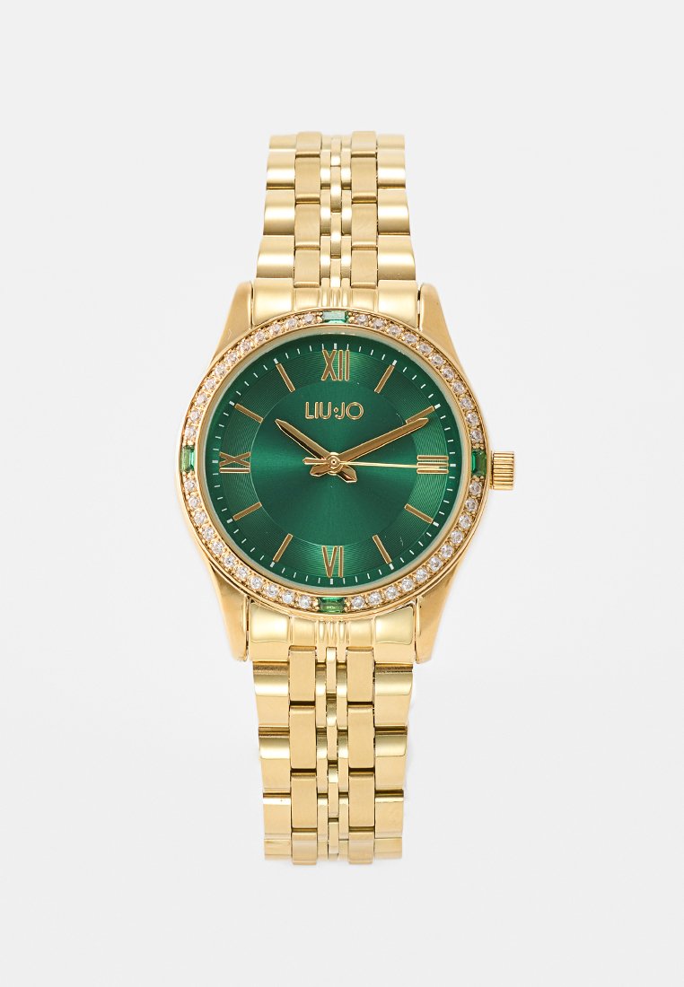 Montre-bracelet dorée avec un cadran vert, des chiffres romains et des accents en cristaux. Elle possède un bracelet métallique à maillons et un boîtier rond.