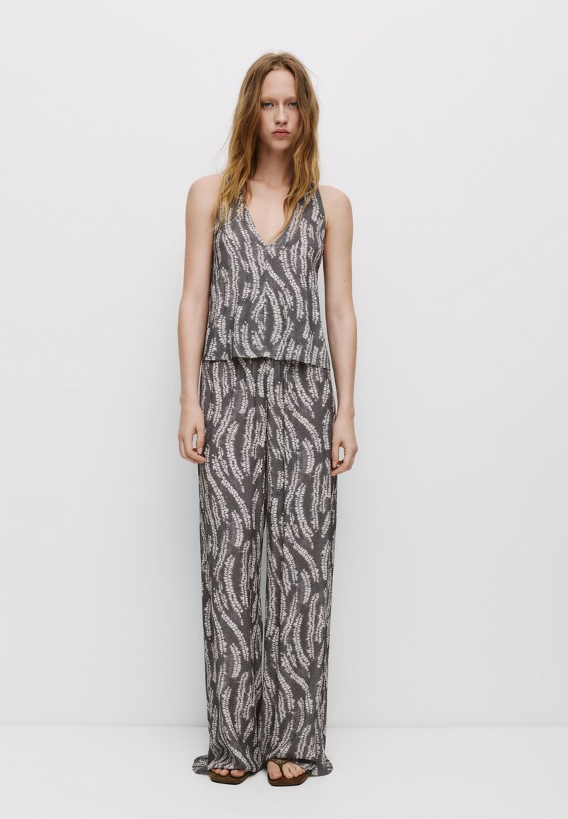 Grijze jumpsuit met een patroon, voorzien van een mouwloze top met een V-hals en losse, wijde broekspijpen. Zacht materiaal met een golfachtig ontwerp.