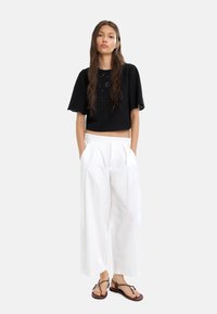Czarny crop top z krótkimi rękawami i kwiecistym haftem, zestawiony z luźnymi białymi spodniami i płaskimi sandałami. Gładki materiał, luźny krój.