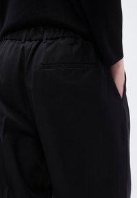 Μαύρο παντελόνι σε στενή γραμμή με ελαστική μέση, διαθέτει πίσω τσέπη και λεία, ματ υφή. Είναι ορατές τσέπες στις πλευρικές ραφές.