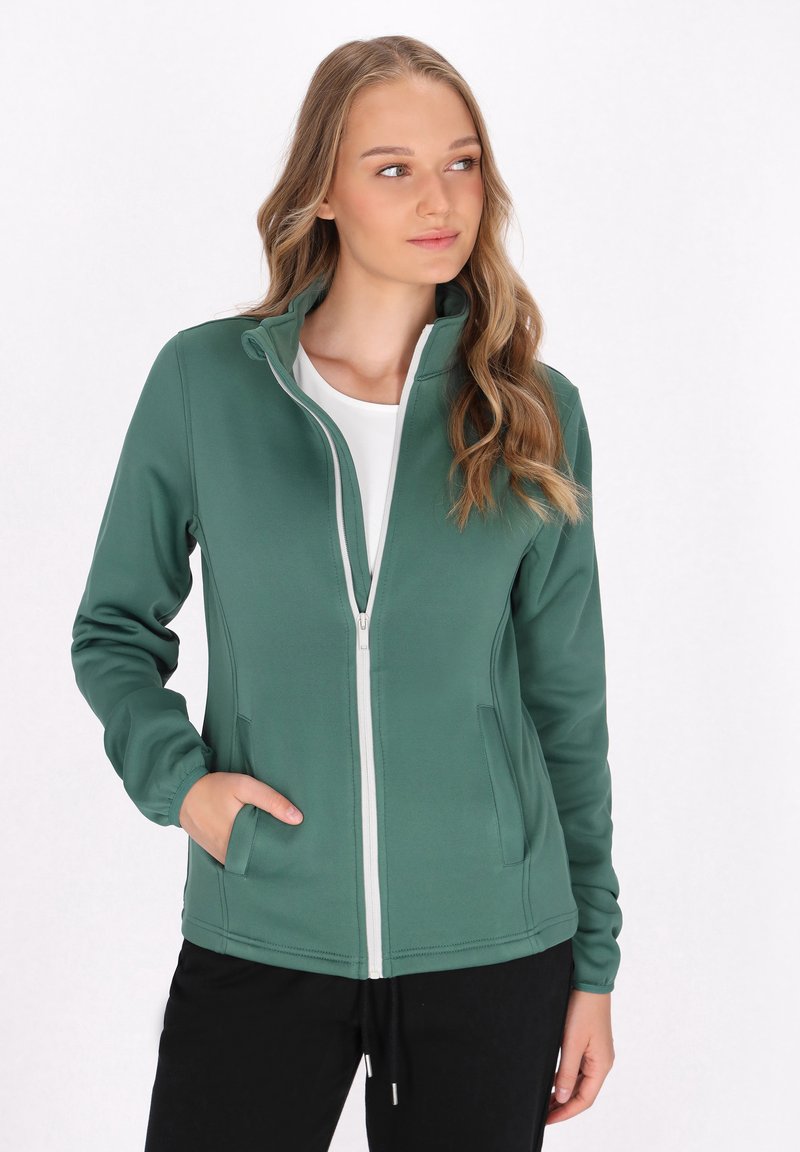 Giacca verde con zip realizzata in tessuto morbido, dotata di colletto alto, zip a contrasto e tasche laterali. Texture liscia con design aderente.