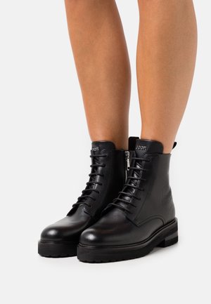Černé kožené kotníkové boty s kulatými špičkami, předním šněrováním a bočními zipy. Mají texturovanou podrážku a logo značky na kotníku.