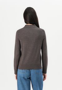 Pull en marron foncé avec col, manches longues, poignets et ourlet côtelés. Porté avec un jean en denim bleu clair, vu de dos sur un fond blanc.