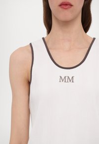 Biely rebrovaný top s hnedým lemovaním, s vyšitým logom "MM" na hrudi. Minimalistický dizajn s zaobleným výstrihom.