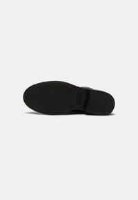 Semelle de chaussure noire avec une texture lisse et mate, forme de bout arrondi et détail de marque subtil. Design plat adapté pour un usage décontracté ou formel.