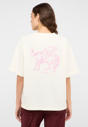 Überdimensionales, cremefarbenes T-Shirt mit einem pinkfarbenen Motiv eines Cowboys, der auf einem Pferd reitet, auf der Rückseite. Kurze Ärmel und lockere Passform.