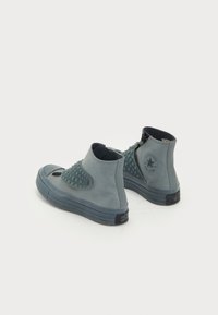 Sneakers de cano alto em material azul mate, com um padrão texturizado de estrelas na lateral e uma sola de borracha com o logótipo no calcanhar.
