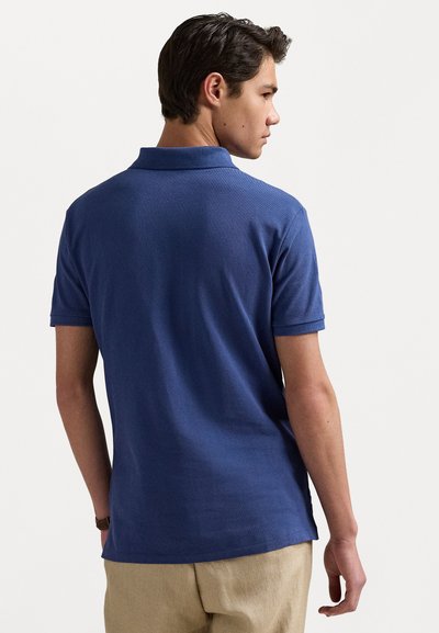 Marineblaues Poloshirt aus strukturiertem Stoff mit kurzen Ärmeln und Kragen. Die Rückansicht zeigt eine lässige Passform und seitliche Belüftungsdetails.