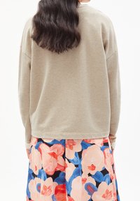 Béžová oversize mikina s nízkými rameny, doplněná květinovou sukní s velkými růžovými a modrými vzory na tmavém podkladu.