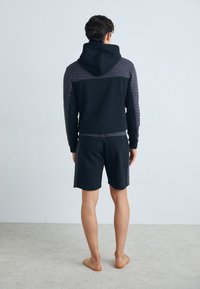 Black hoodie with patterned shoulder and sleeve accents, paired with black shorts. Smooth texture, relaxed fit, and no visible hardware.