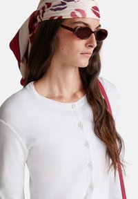 Bílý kardigan s knoflíky, měkká textura, doplněný o vzorovaný hedvábný šátek a sluneční brýle z tmavého želvovinového vzoru. Příjemné detaily doplňují celý outfit.