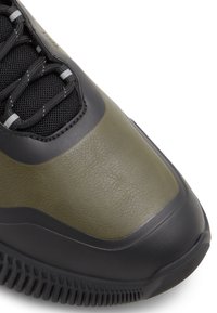 Zapatillas verdes y negras con parte superior de cuero texturizado, detalles de malla y una suela de goma robusta con patrones de relieve prominentes.