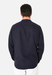 Camicia a maniche lunghe blu navy con polsini a bottoni, orlo dritto e dettagli sulla spalla posteriore. Realizzata in tessuto leggero, presenta una texture liscia.