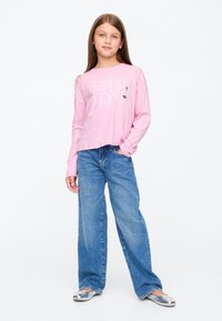 Hosszú ujjú rózsaszín ing "SISTERHOOD" grafikával, bőszárú kék farmerrel és ezüst színű, könnyen felvehető cipővel párosítva. Sima anyag, laza fazon.