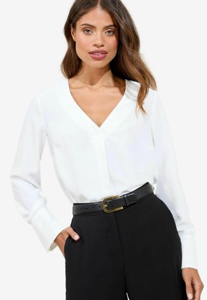Camicia bianca a maniche lunghe con scollatura a V, abbinata a pantaloni neri a vita alta e una cintura nera con una fibbia dorata.